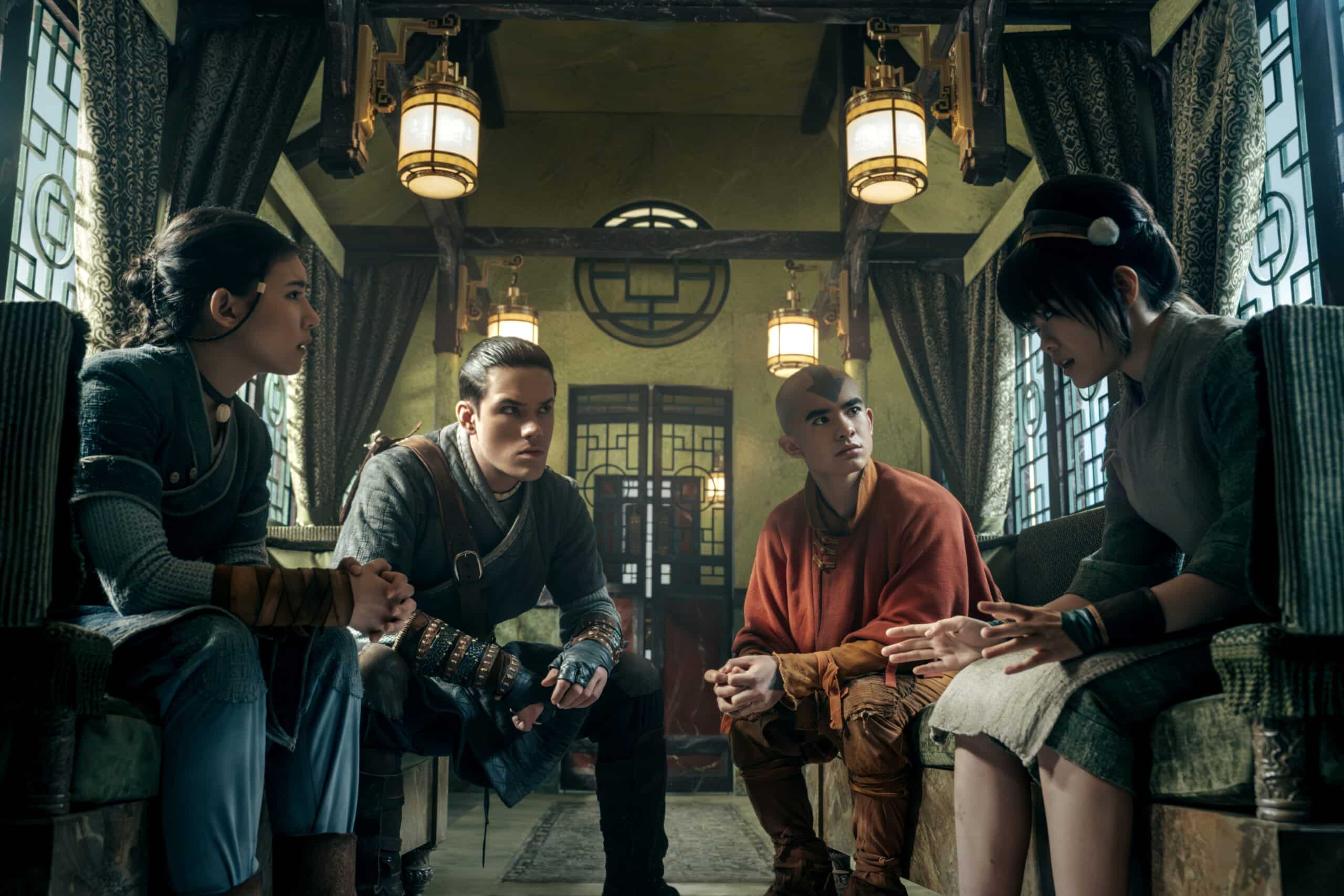 "A young girl with black hair, a young man with black hair, a young boy with a tattoo of an arrow on his forehead, and another young girl with black hair sit together in a train car."